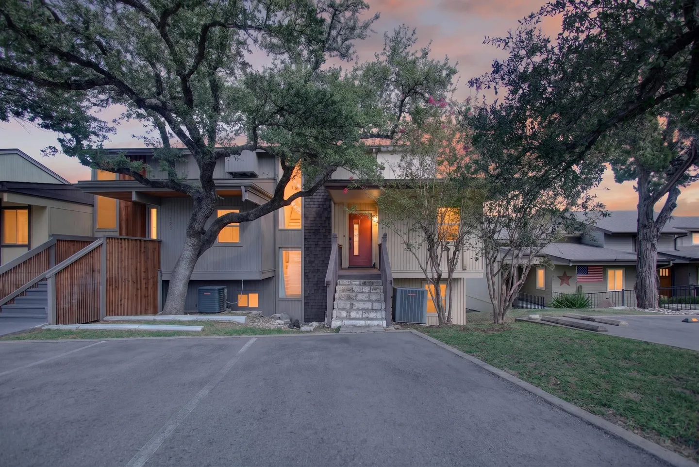Exterior view of a multi-level condo or townhouse at dusk with a paved parking area in the foreground.