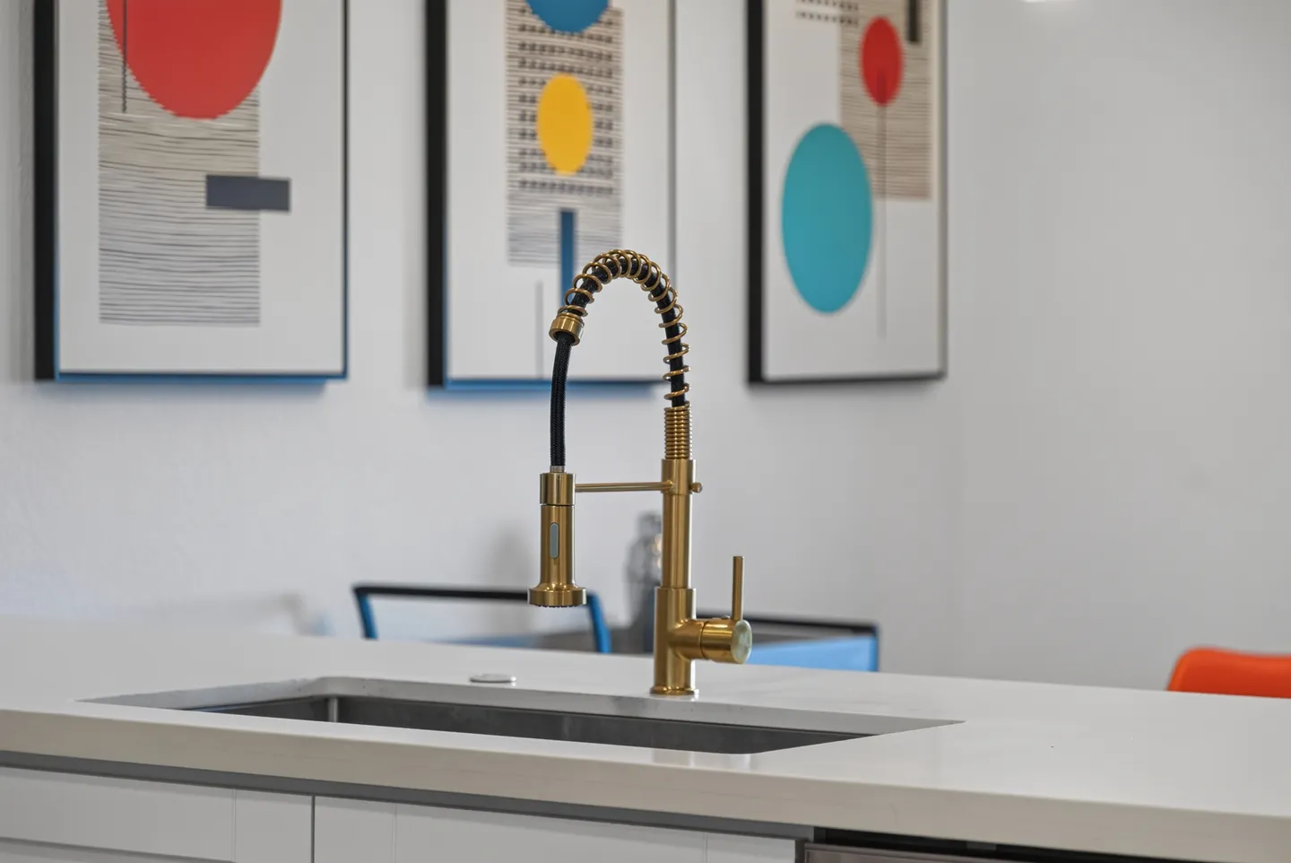 Close-up of a modern gold kitchen faucet and undermount sink with framed geometric artwork hanging in the background.