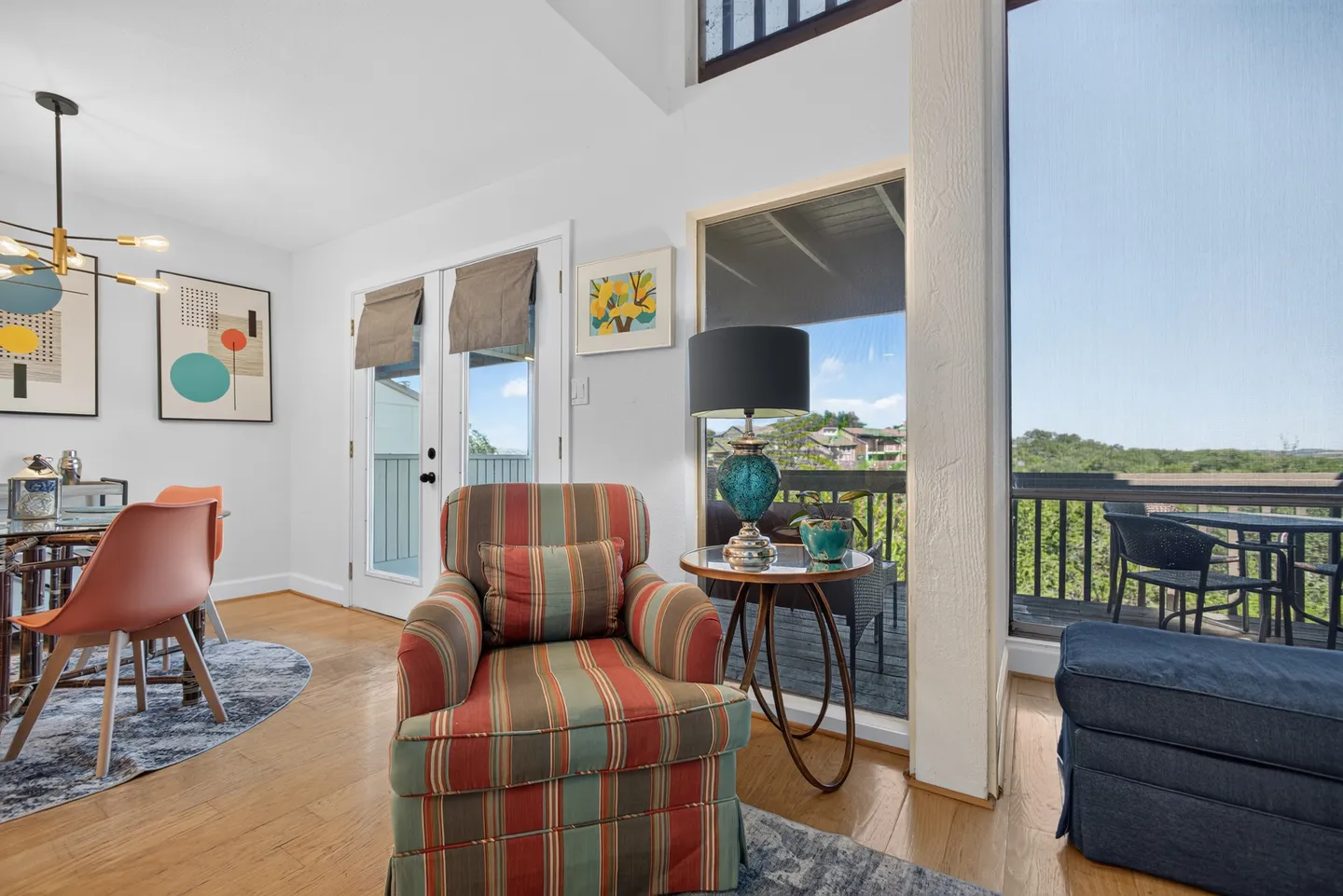Living area corner featuring a striped armchair next to a balcony doorway with dining furniture to the left.