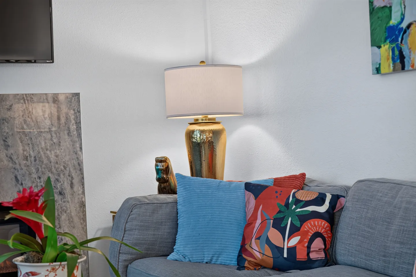 Close-up of a living room sofa with colorful throw pillows, a gold table lamp, and an indoor plant.