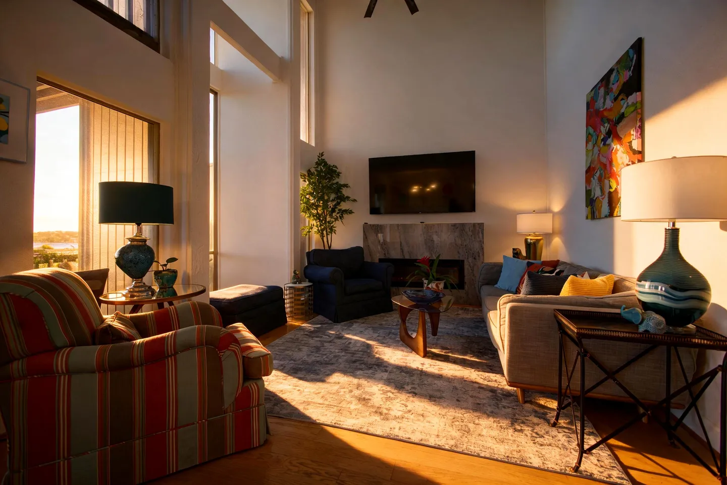 Living room with high ceilings, tall windows bathed in sunlight, a fireplace, television, and varied armchair seating.
