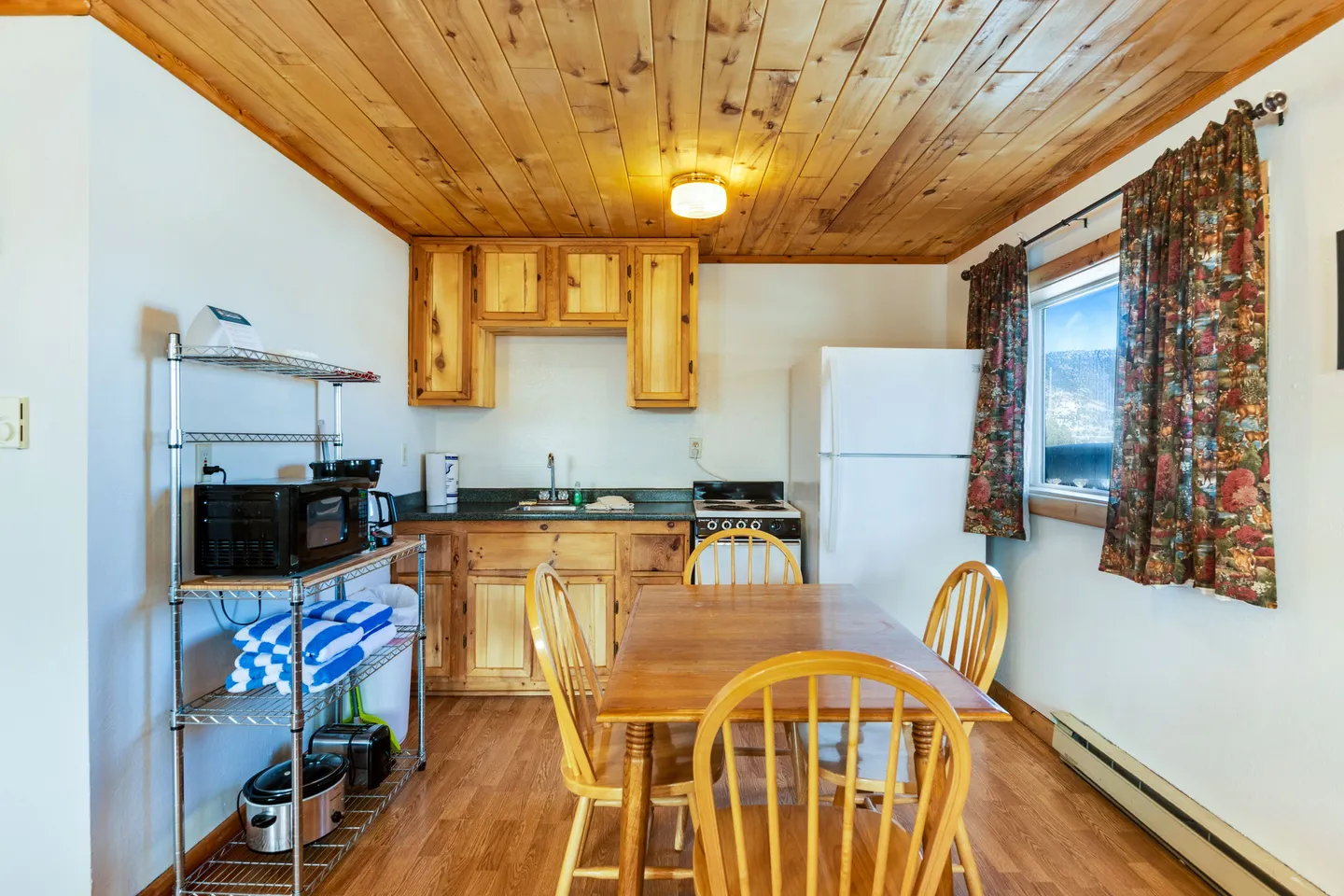Kitchen and dining area featuring wood-paneled ceiling, light wood cabinets, dining table with chairs, and a metal storage rack.