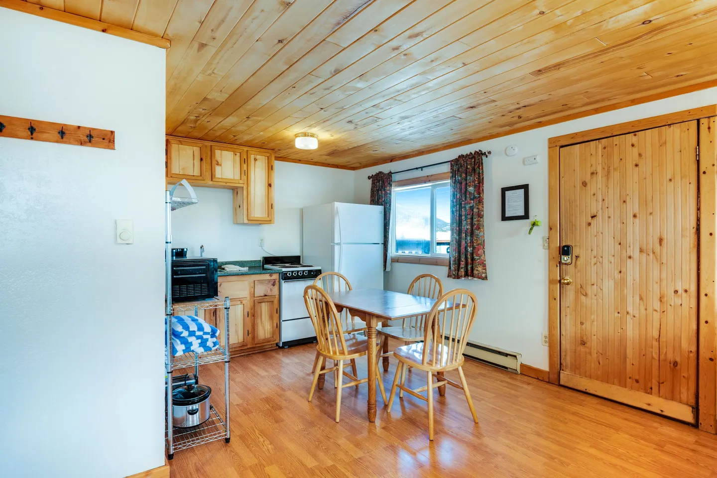 Kitchen and dining area featuring wood plank ceilings, wood paneled doors, a wooden dining table with four chairs, and kitchen appliances.