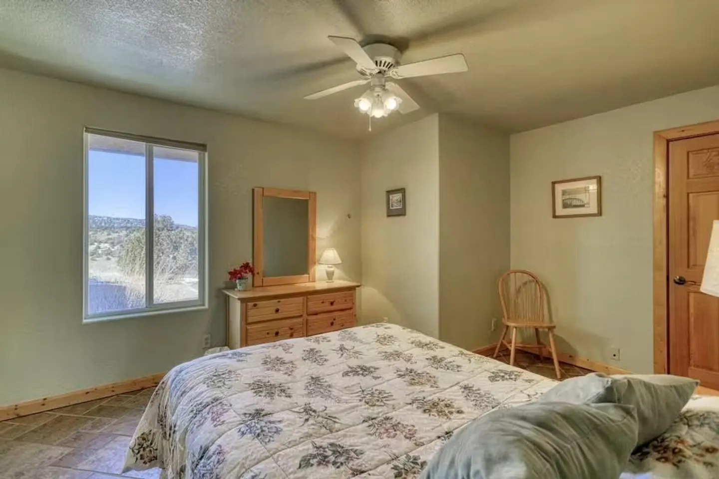 Bedroom featuring a bed with a floral quilt, a dresser with mirror, and a window showing outdoor scenery.