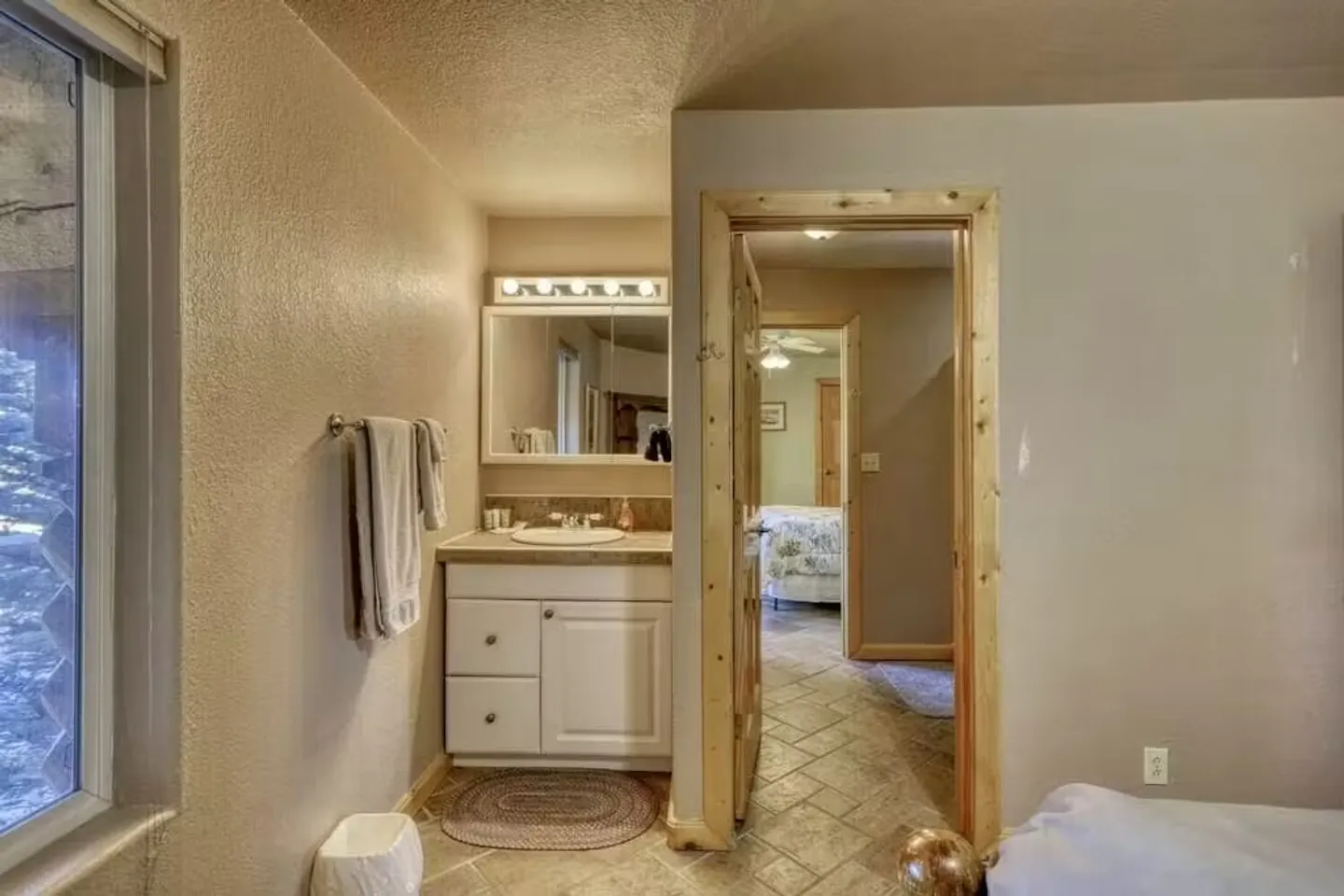 Bathroom vanity with mirror and white cabinet next to an open doorway leading to a hallway and bedroom.