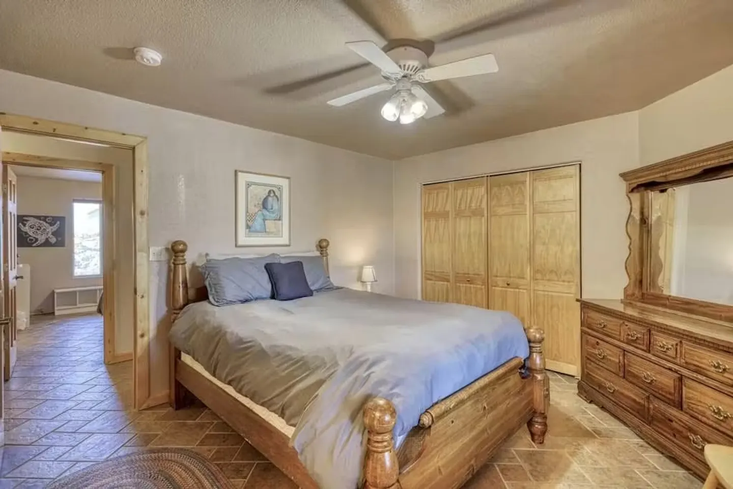 Bedroom featuring a wooden frame bed, matching dresser with mirror, tiled floor, ceiling fan, and folding closet doors.