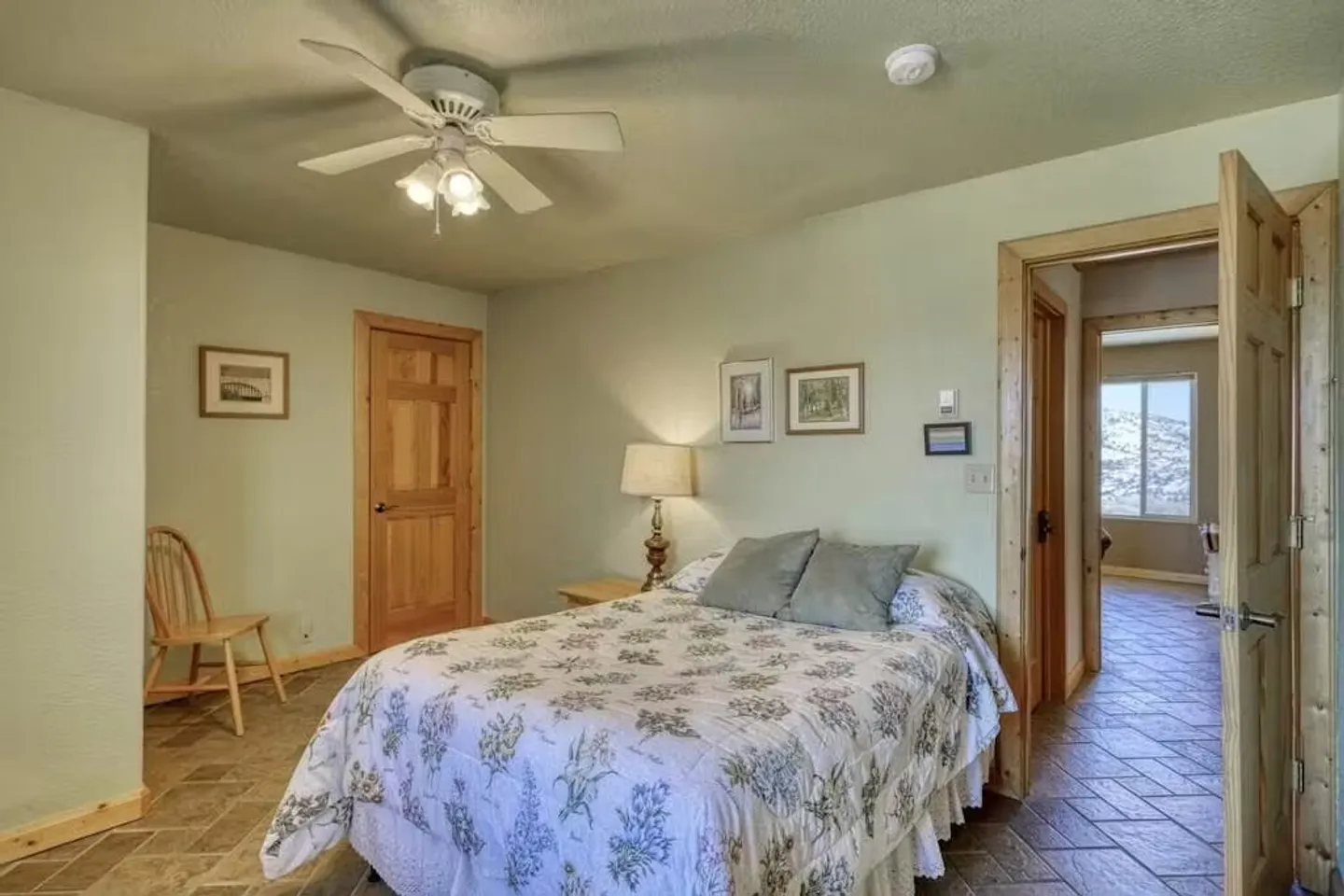 Bedroom with a patterned floral quilt on the bed, tiled floor, ceiling fan, wooden doors, and light green walls.
