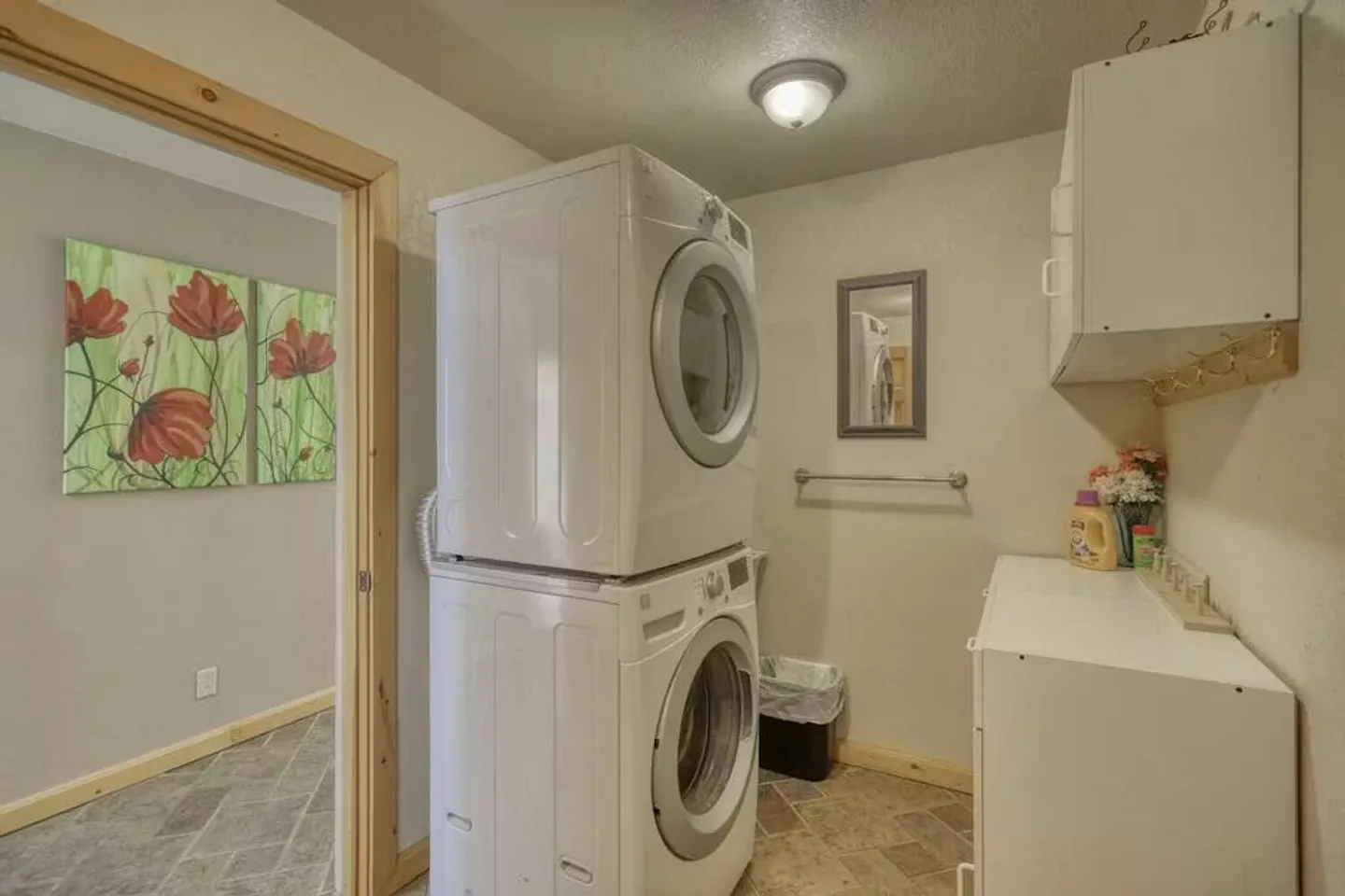 Dedicated indoor laundry room featuring a stacked front-loading washer and dryer, white cabinets, and tiled flooring.