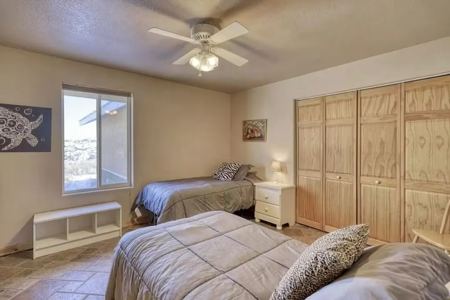 Bedroom with two single beds, tiled flooring, a ceiling fan, a window, and large folding closet doors.