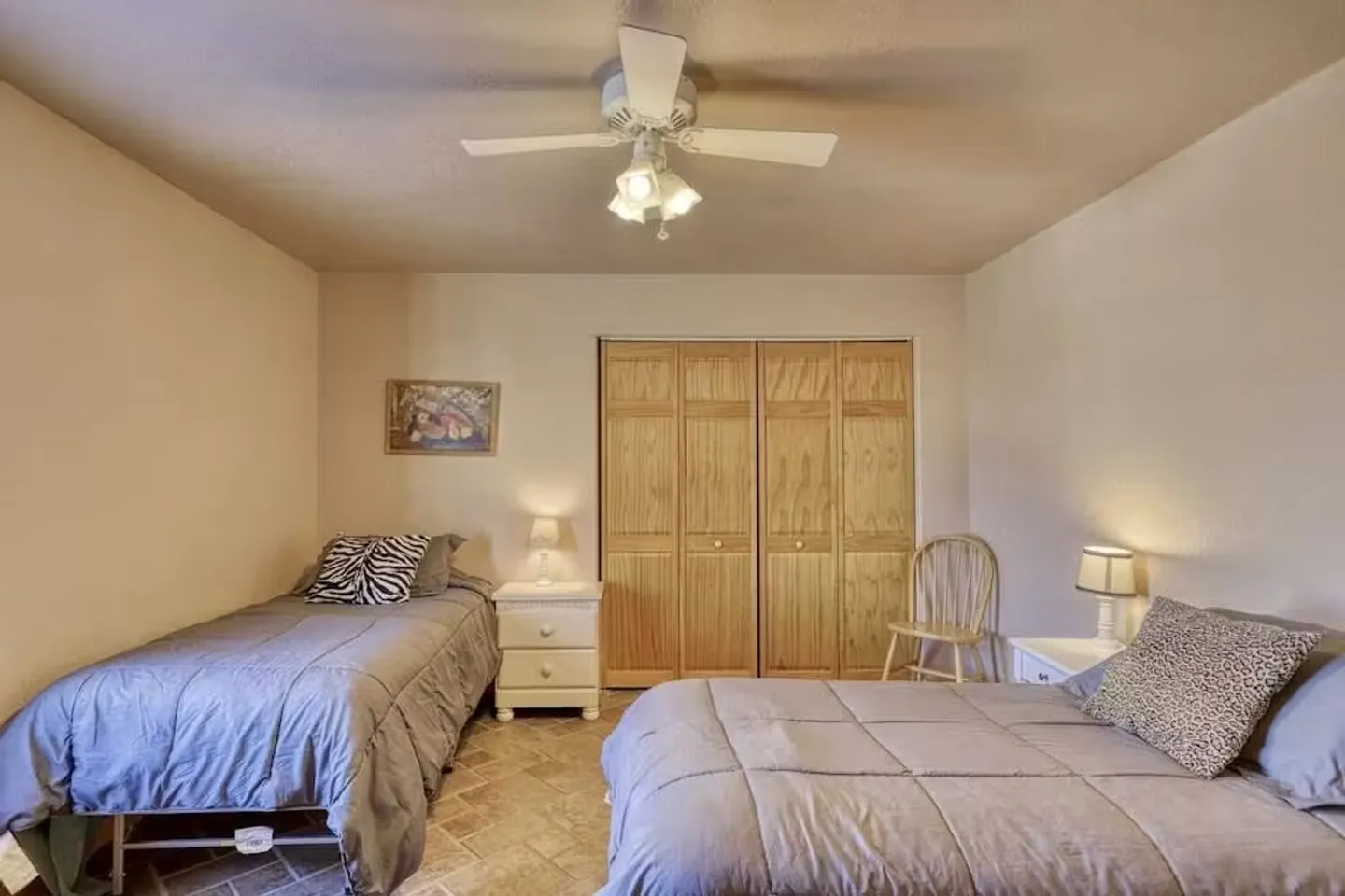 Bedroom featuring two beds with gray bedding, a white nightstand, wooden closet doors, and a ceiling fan.