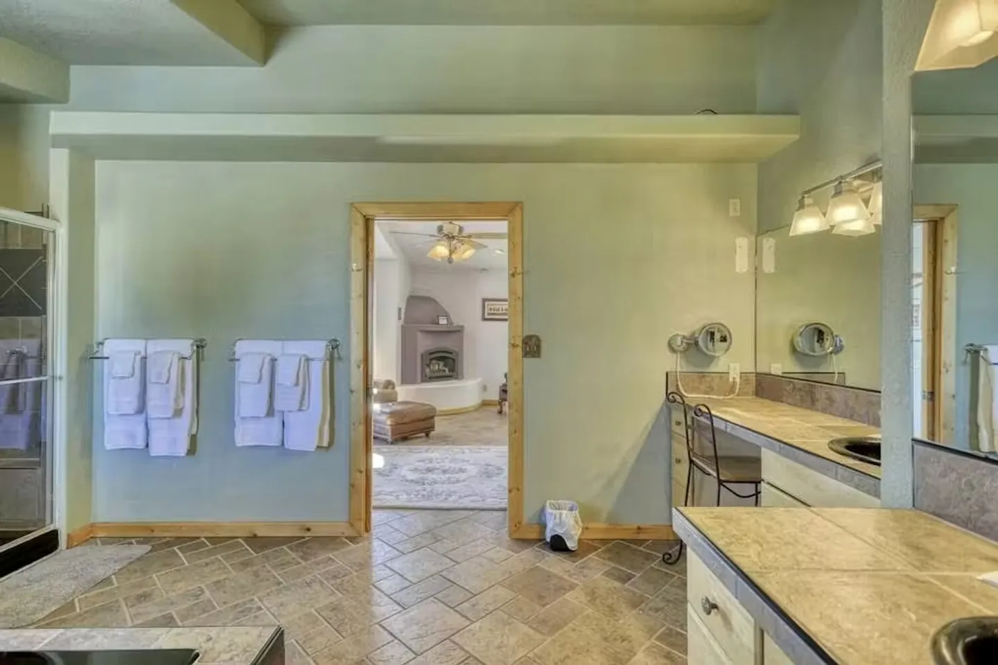 Bathroom with tile floors, vanity area, towel racks, and a doorway looking into an adjacent room with a kiva fireplace.
