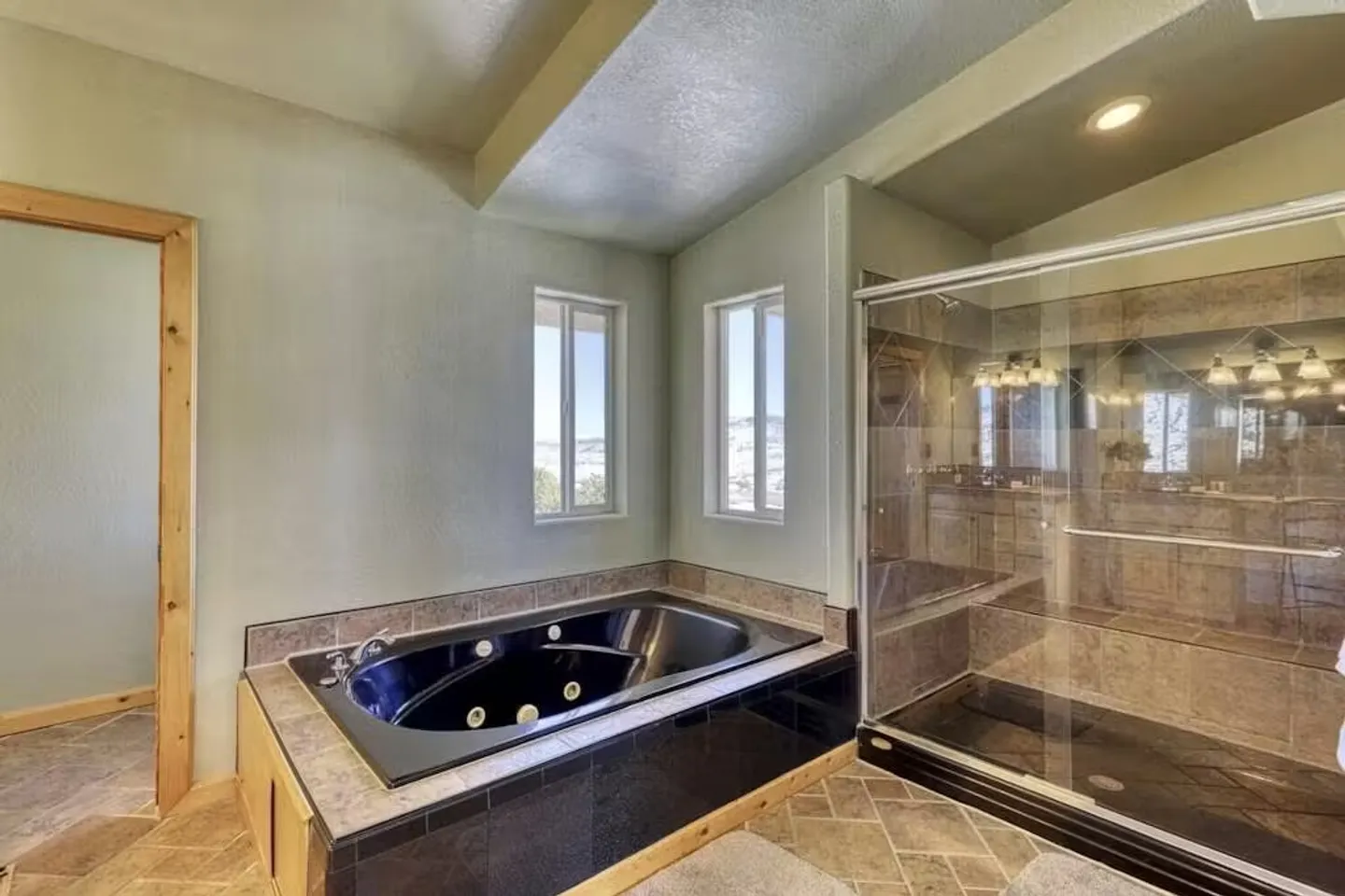 Bathroom featuring a black sunken jetted tub next to two windows and a glass-enclosed walk-in shower with tiled walls.