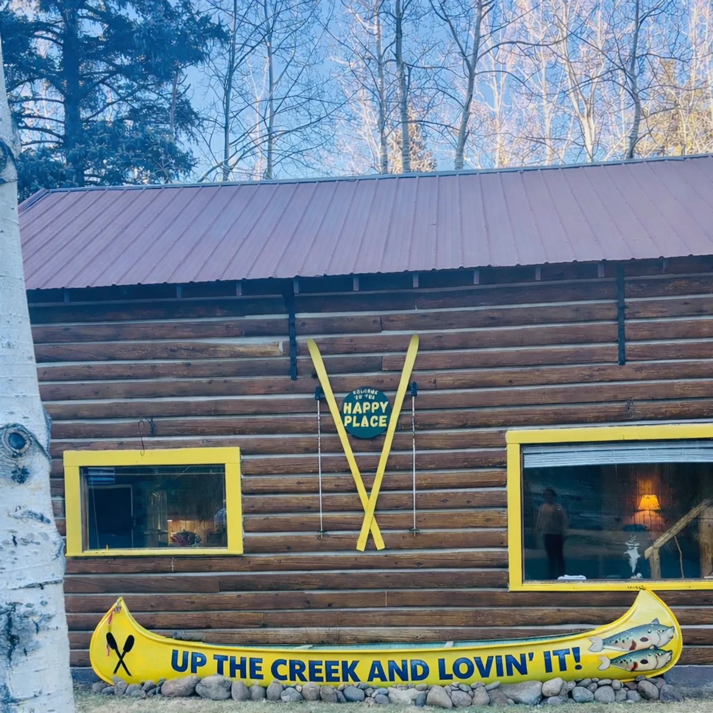 Exterior log cabin wall featuring a yellow canoe sign, yellow skis, and yellow window frames.