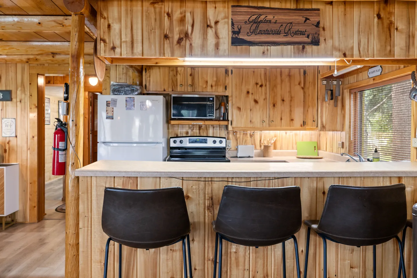 Kitchen counter with three modern barstools in a rustic cabin featuring knotty pine wood paneled walls and cabinets.