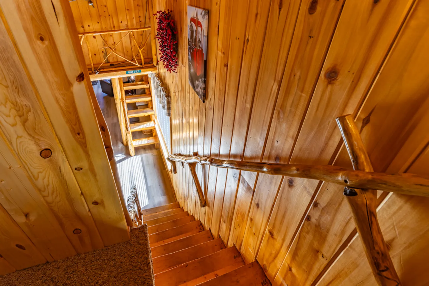 Looking down a wooden staircase with log-style handrails inside a wood-paneled cabin.