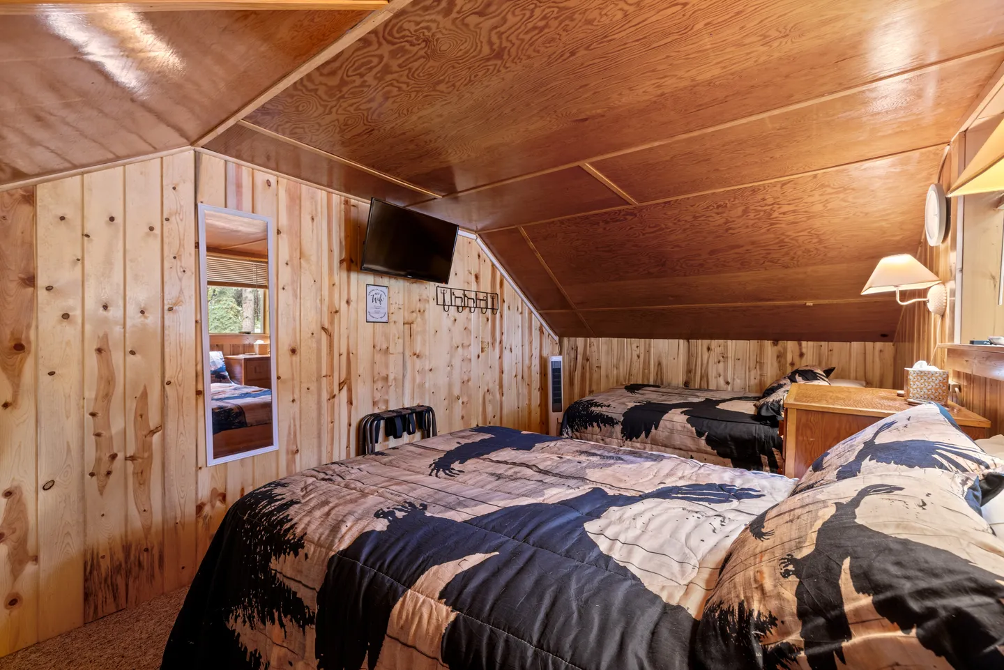 Bedroom with angled wood ceiling, wood-paneled walls, and two beds topped with patterned quilts.