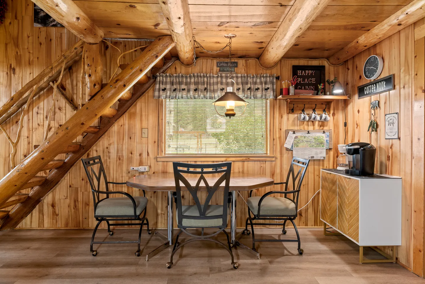 Dining area with wood-paneled walls, an oval table with chairs, an open-tread log staircase, and a coffee bar cabinet.