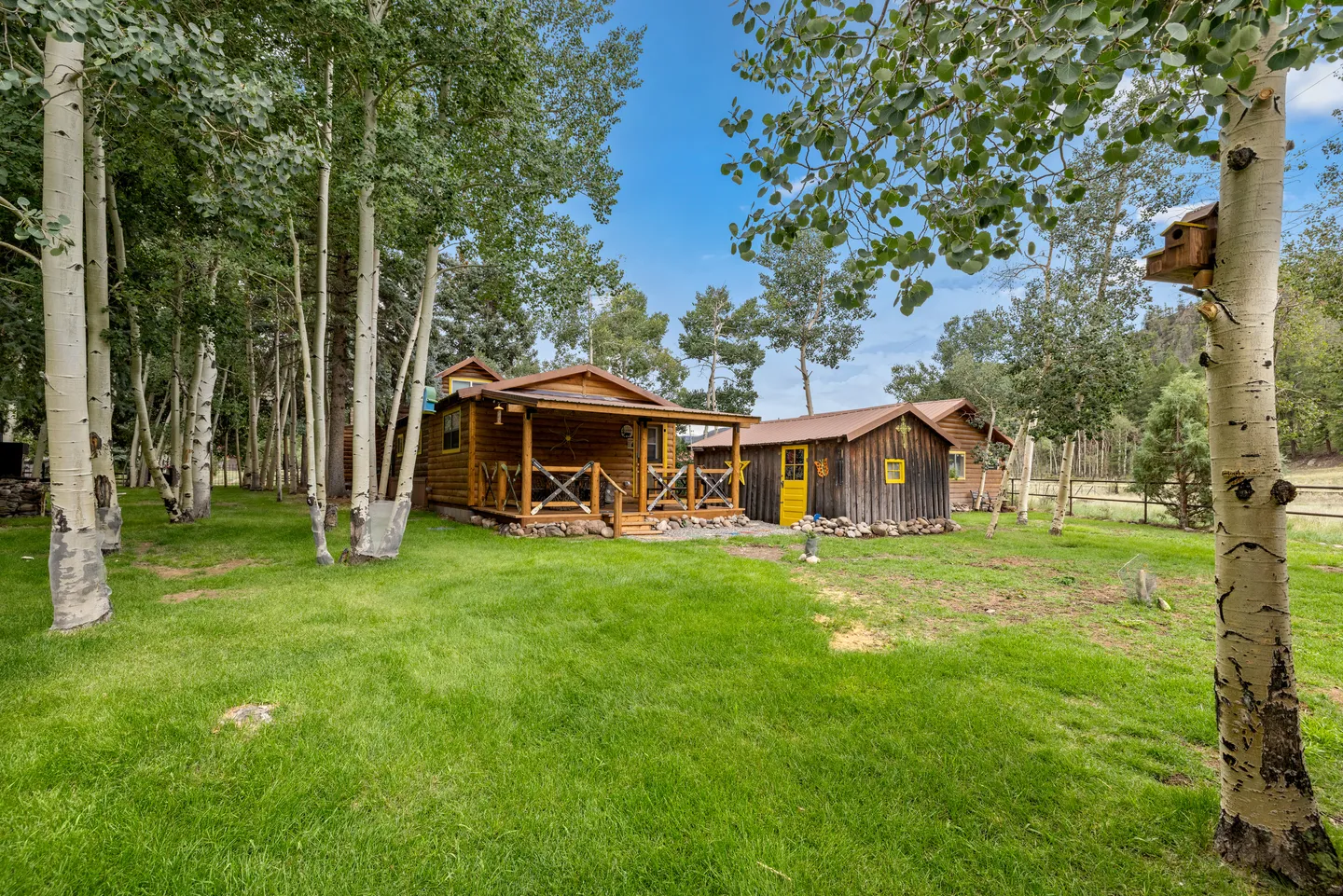 Exterior view of rustic log cabins situated on a grassy lawn surrounded by aspen trees.
