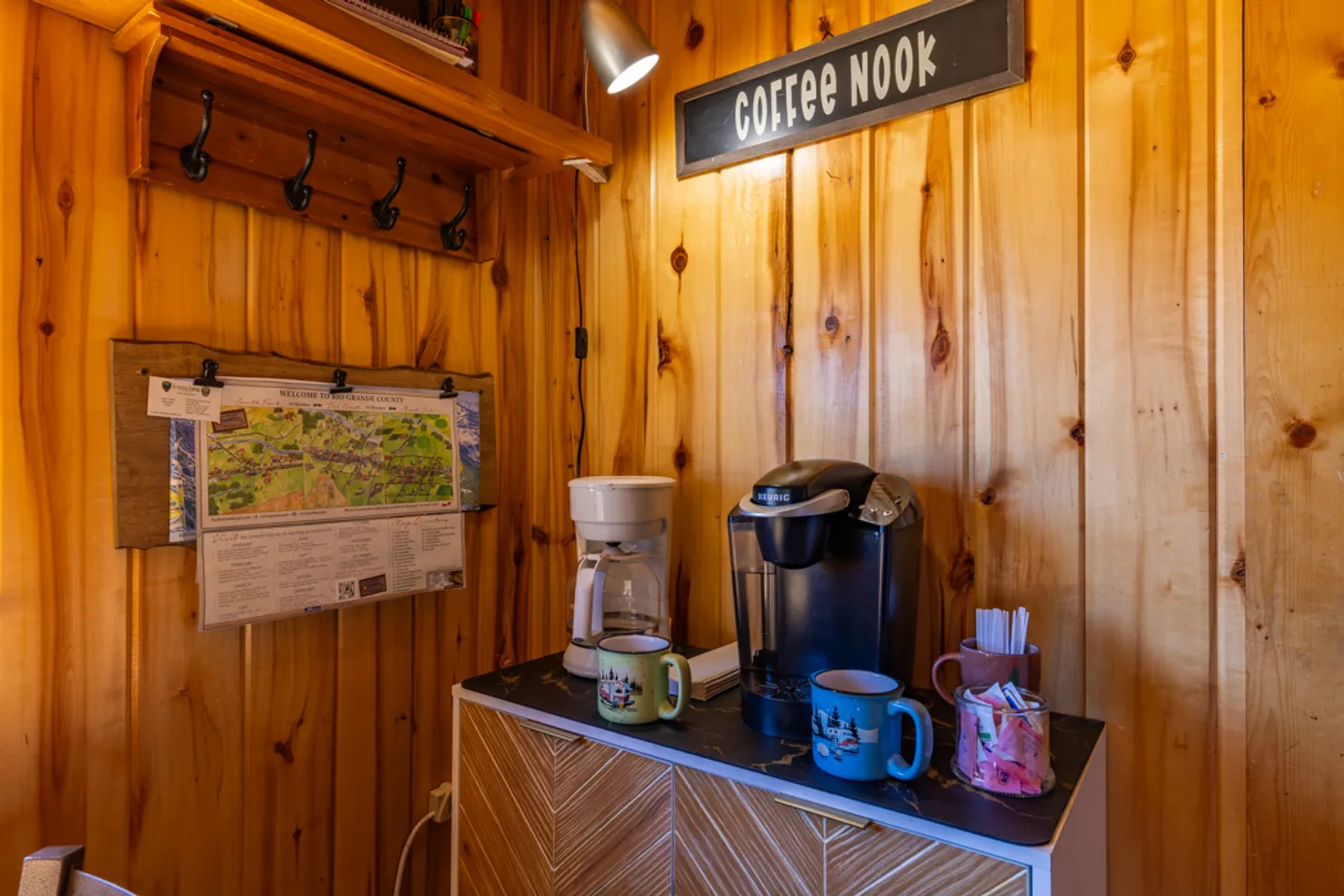 Dedicated coffee nook set against wood-paneled walls, featuring a drip coffee maker, single-serve machine, mugs, and a sign overhead.