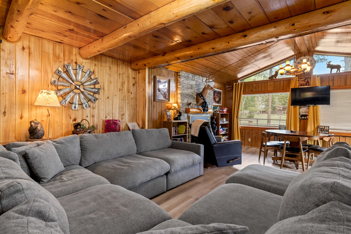 Living room with wood paneled walls, log beam ceiling, and a large gray sectional sofa.