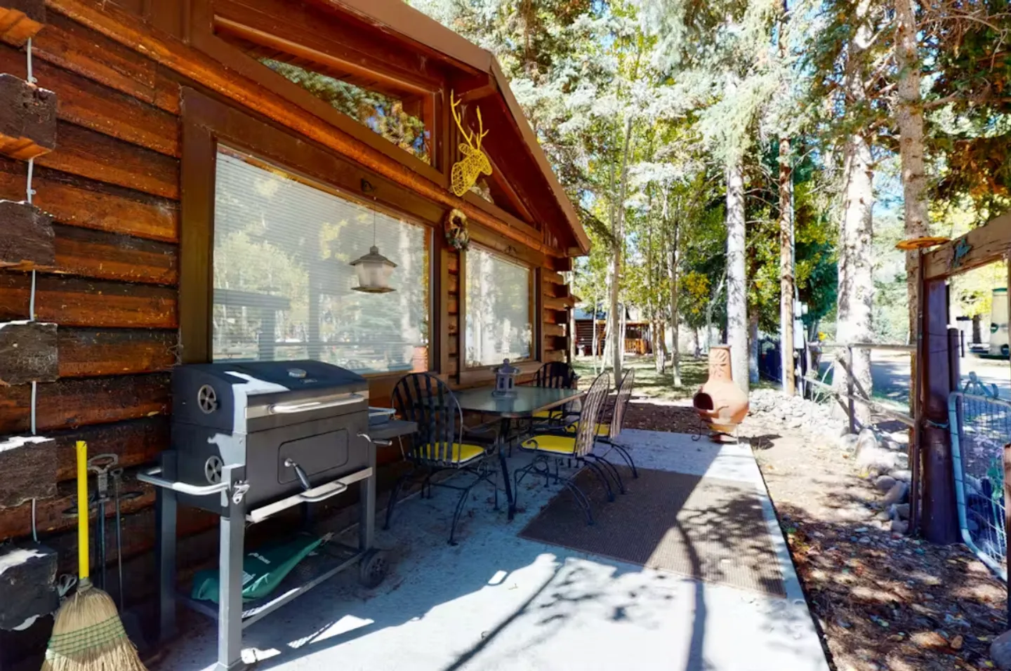 Concrete outdoor patio alongside a log cabin with a grill, dining table and chairs, and a chiminea.