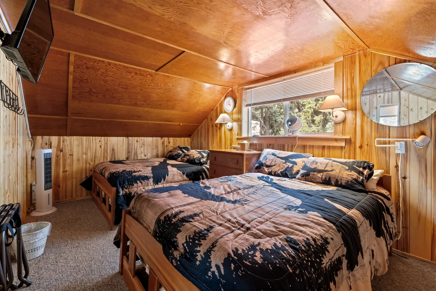 Bedroom with angled wood-paneled ceiling, knotty pine walls, two beds with bear-motif quilts, and a window.