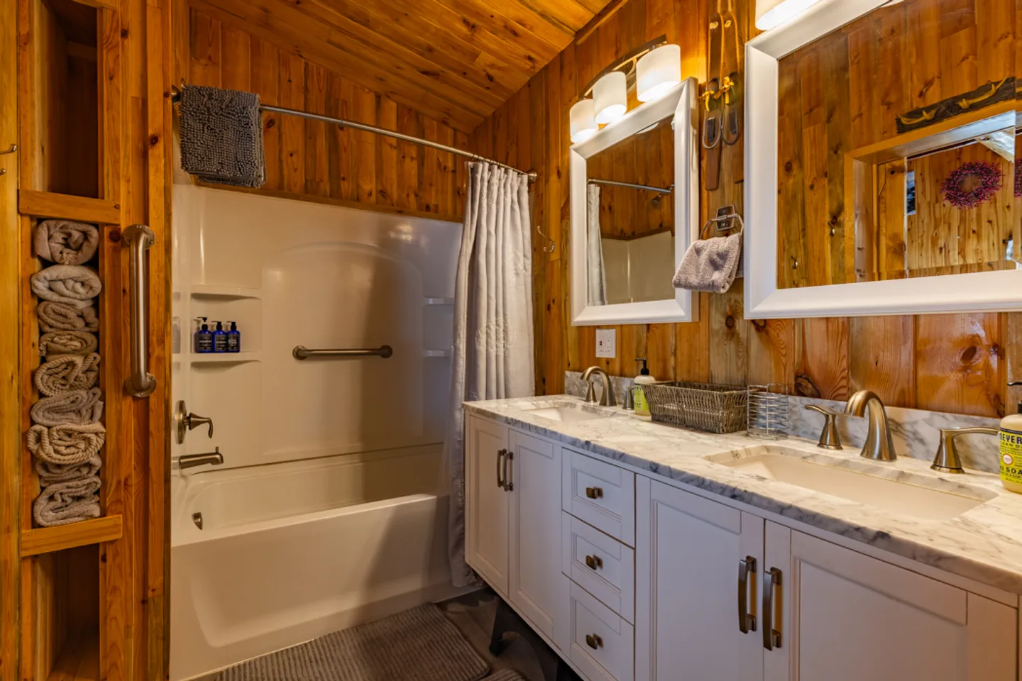 Bathroom with wood-paneled walls, a double vanity with white cabinets, and a white bathtub-shower combo.