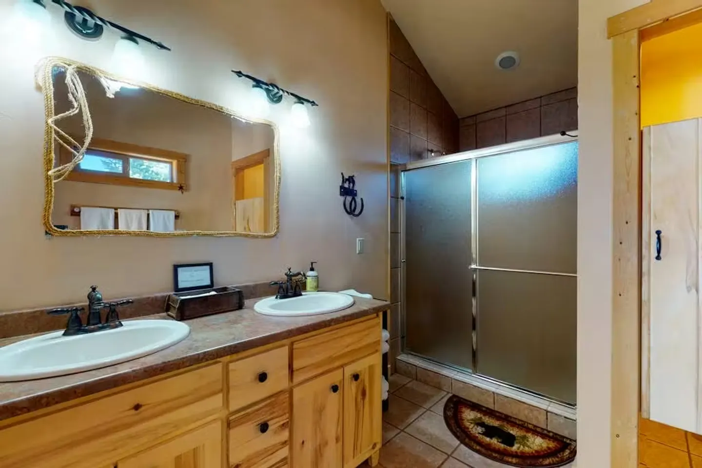Bathroom with a double-sink rustic wood vanity, a rope-trimmed mirror, and a walk-in shower with sliding frosted glass doors.