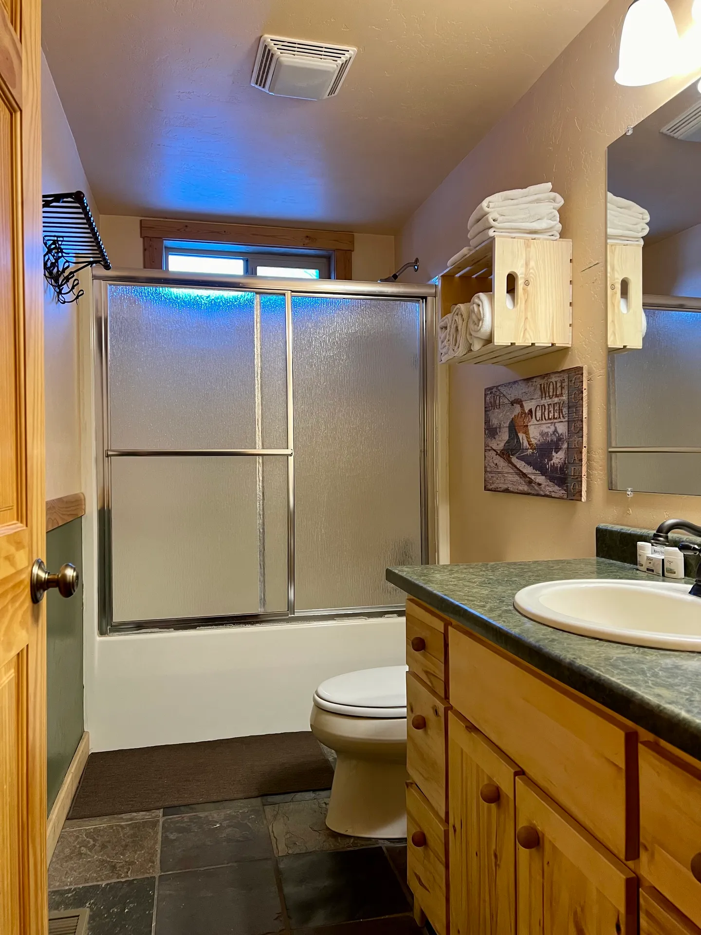 Bathroom featuring a vanity with a green countertop, toilet, and bathtub with sliding frosted glass doors.