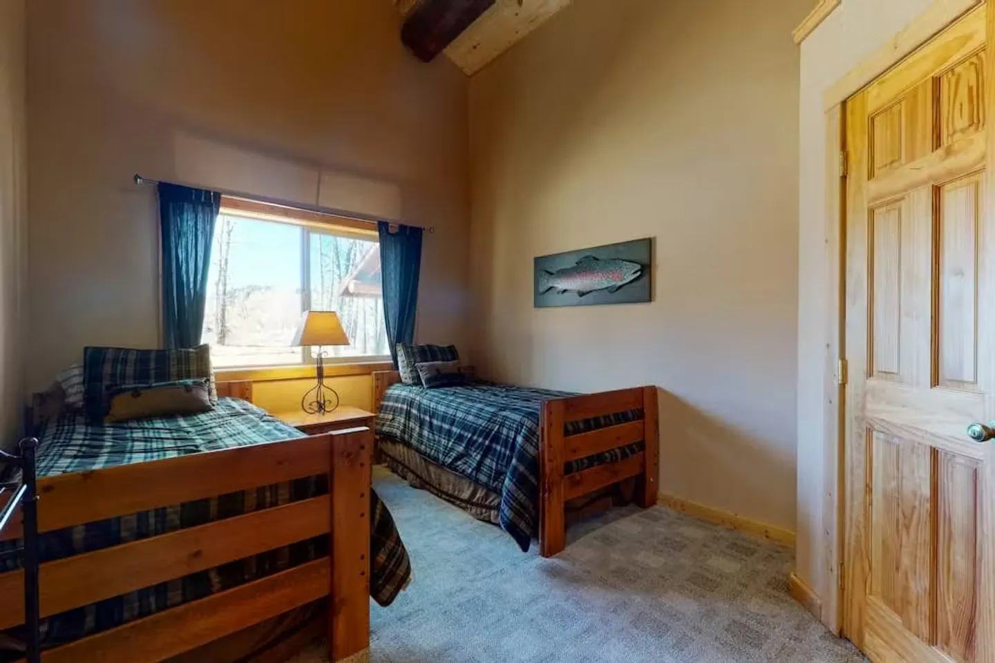 Bedroom with two wooden twin beds with plaid bedding, a window with curtains, and high vaulted ceiling with an exposed log beam.