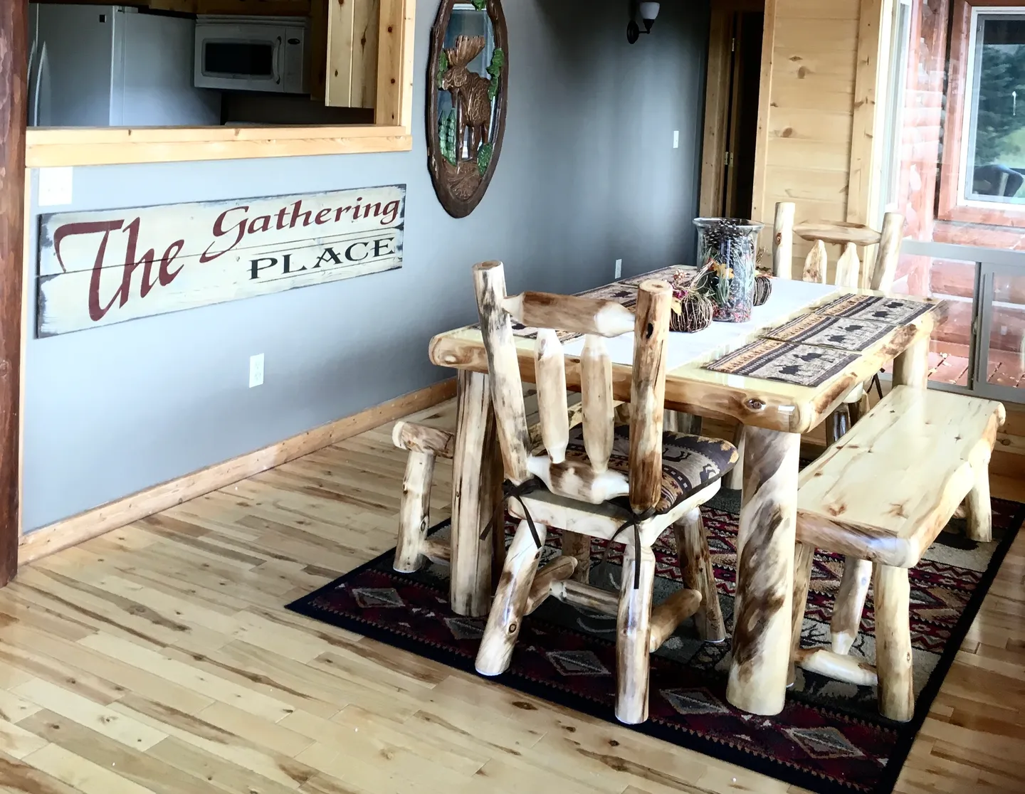 Dining area featuring a rustic log table, log chairs, benches, and hardwood floors adjacent to a kitchen pass-through.