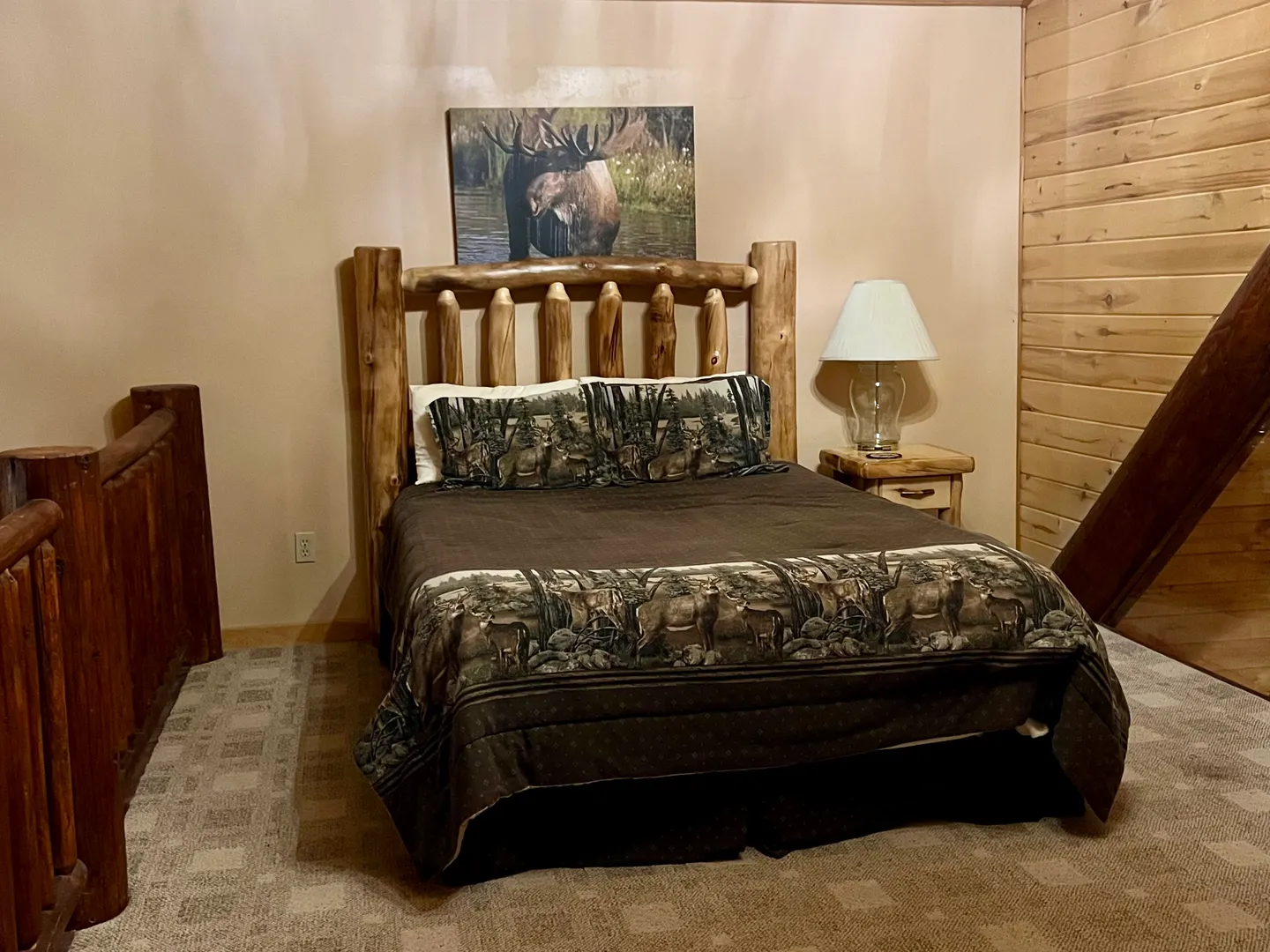 Bedroom featuring a log-style headboard bed with wildlife-themed bedding next to a nightstand with a lamp.
