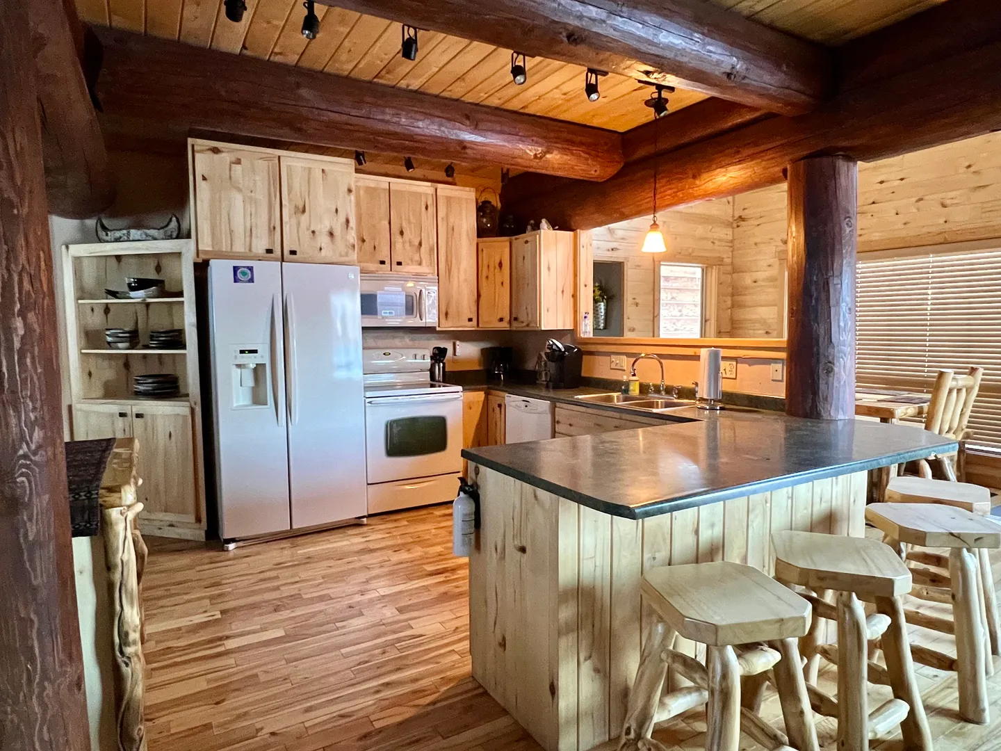 Kitchen in a log-style home with light wood cabinets, white appliances, and an island with rustic wooden bar stools.