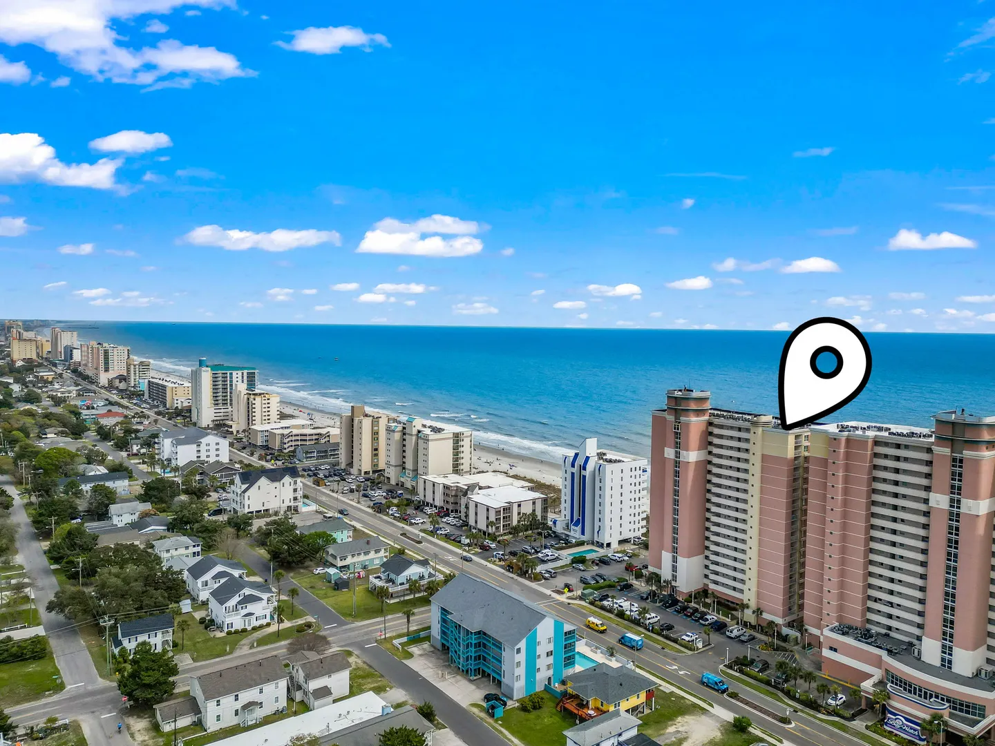 Aerial view of a coastal strip featuring high-rise buildings and residential houses along a sandy beach and ocean.