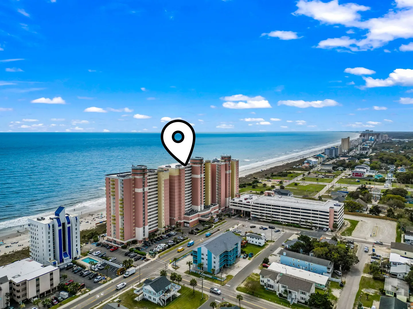 Aerial view of an oceanfront high-rise resort building marked by a location pin, situated along the beach and coastline.