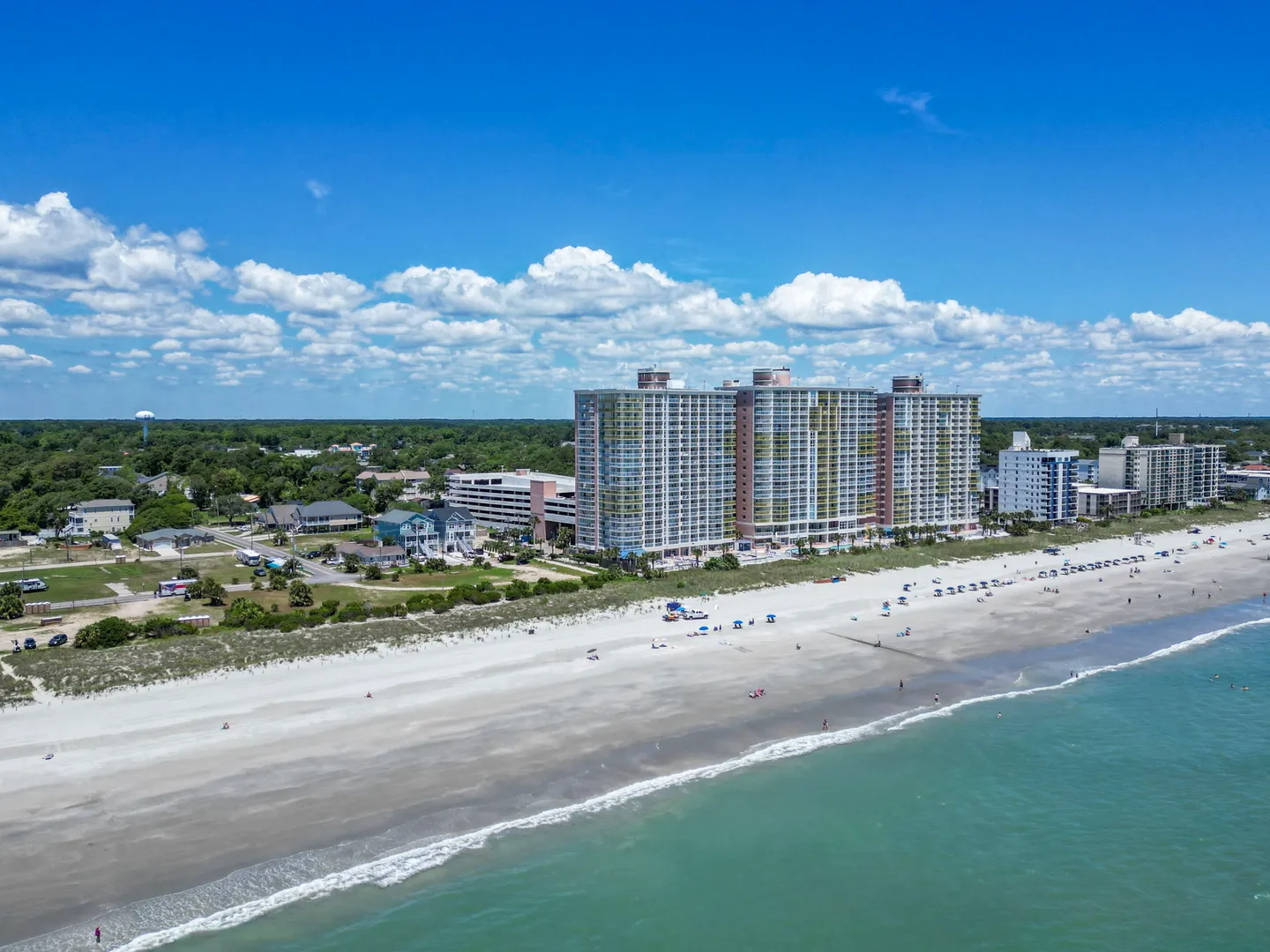 Aerial view of a multistory beachfront condominium building beside a wide sandy beach and ocean waters.