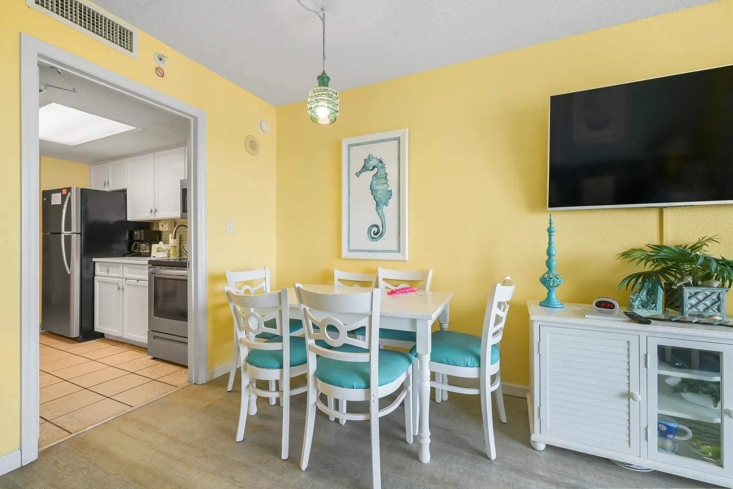 Dining area with a white table and chairs next to bright yellow walls and a view into the kitchen.
