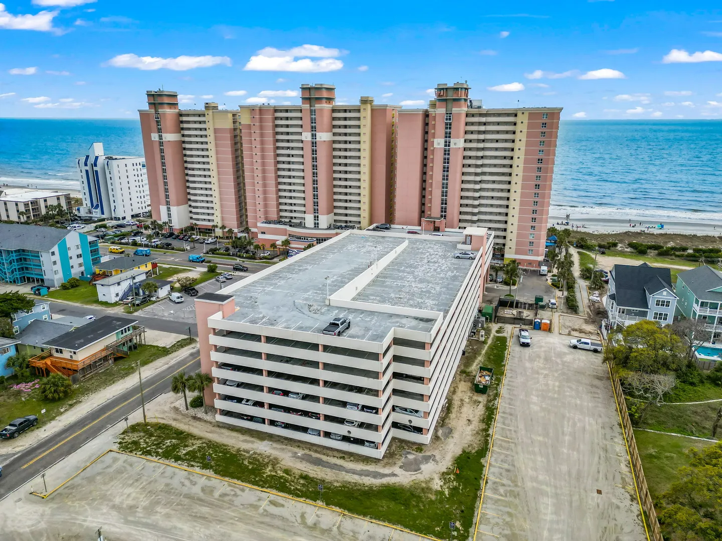 Aerial view of a multistory parking garage in front of a high-rise oceanfront condominium building and the beach.