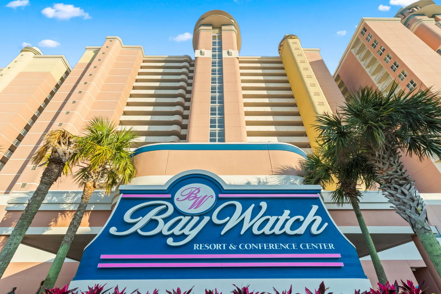 Low-angle view of the exterior entrance sign for Bay Watch Resort and Conference Center in front of a multi-story building.