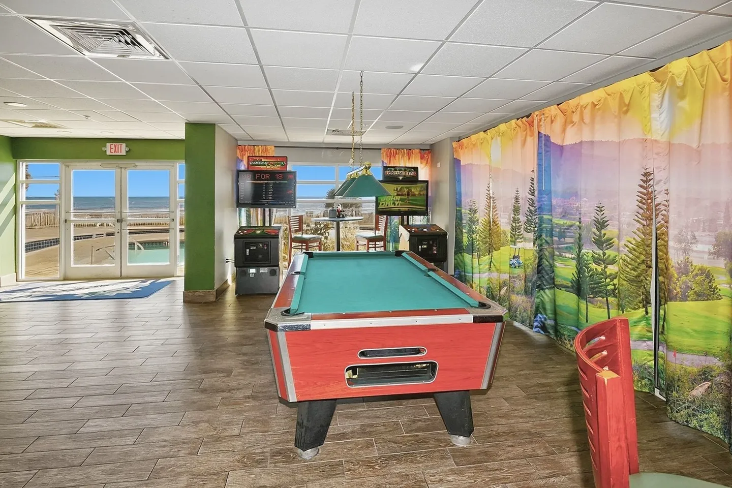 Game room featuring a billiards table, arcade machines, and glass doors looking out to an oceanfront pool deck.