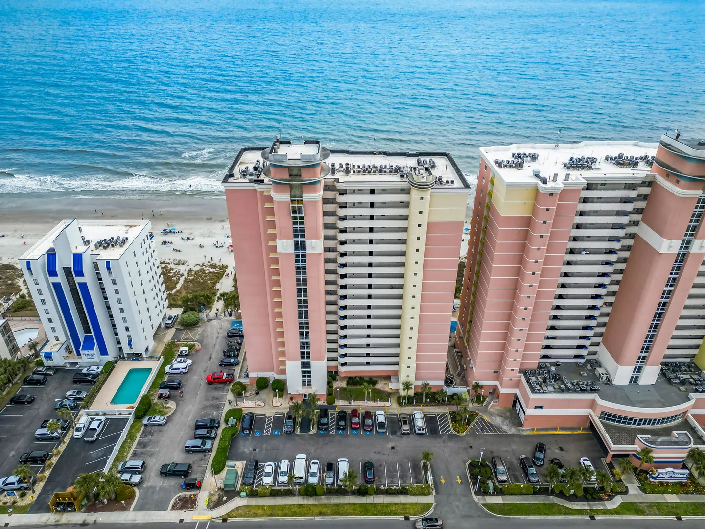 Aerial view of high-rise oceanfront resort towers overlooking a sandy beach and blue ocean.