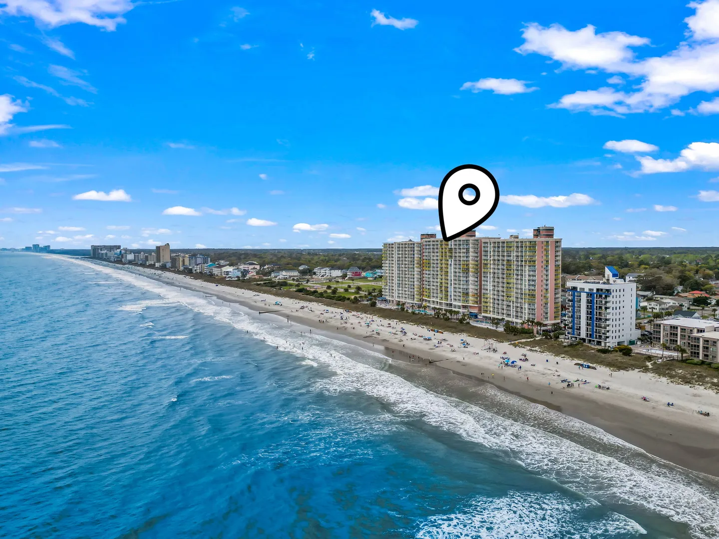 Aerial view of an oceanfront high-rise building alongside a sandy beach and blue ocean waters.
