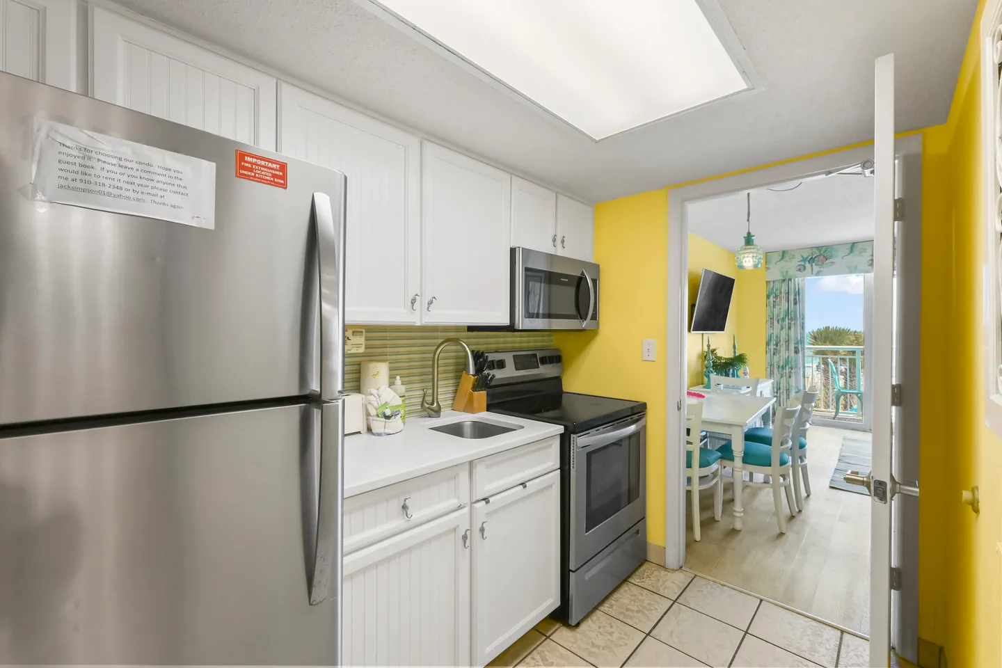 A kitchen with white cabinets, stainless steel appliances, and yellow walls leading into a dining area.