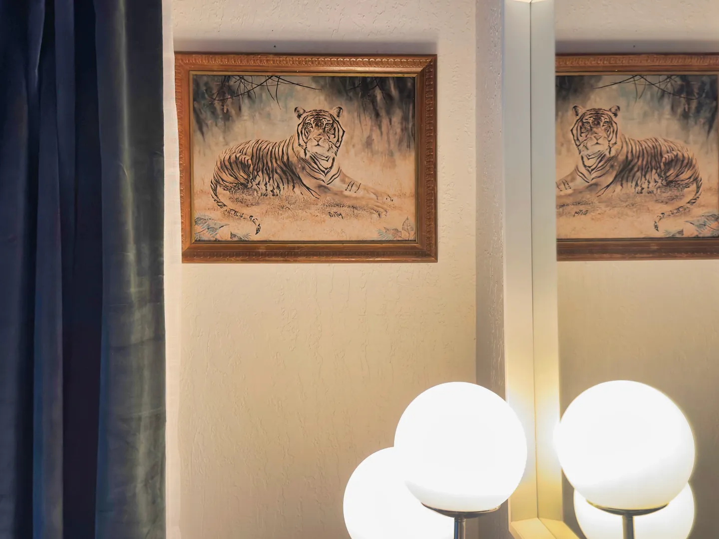 Framed artwork of a tiger hanging on a wall next to a mirror and glowing globe lights.