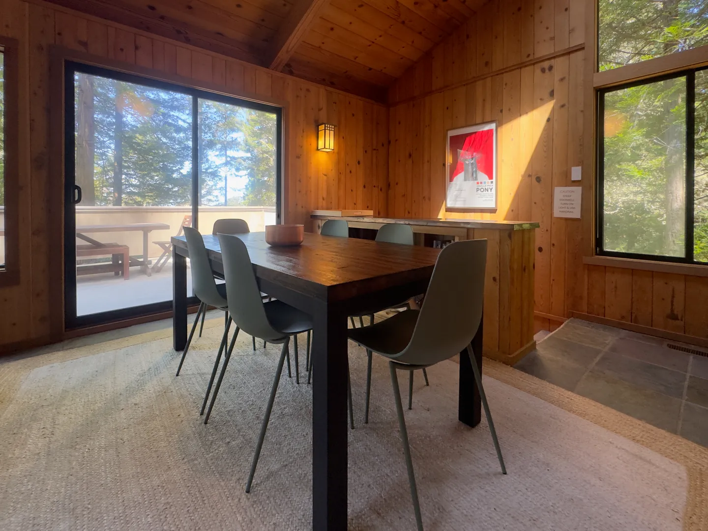 Dining area with dark wood dining table, modern chairs, wood-paneled walls, and sliding glass door leading to a balcony.
