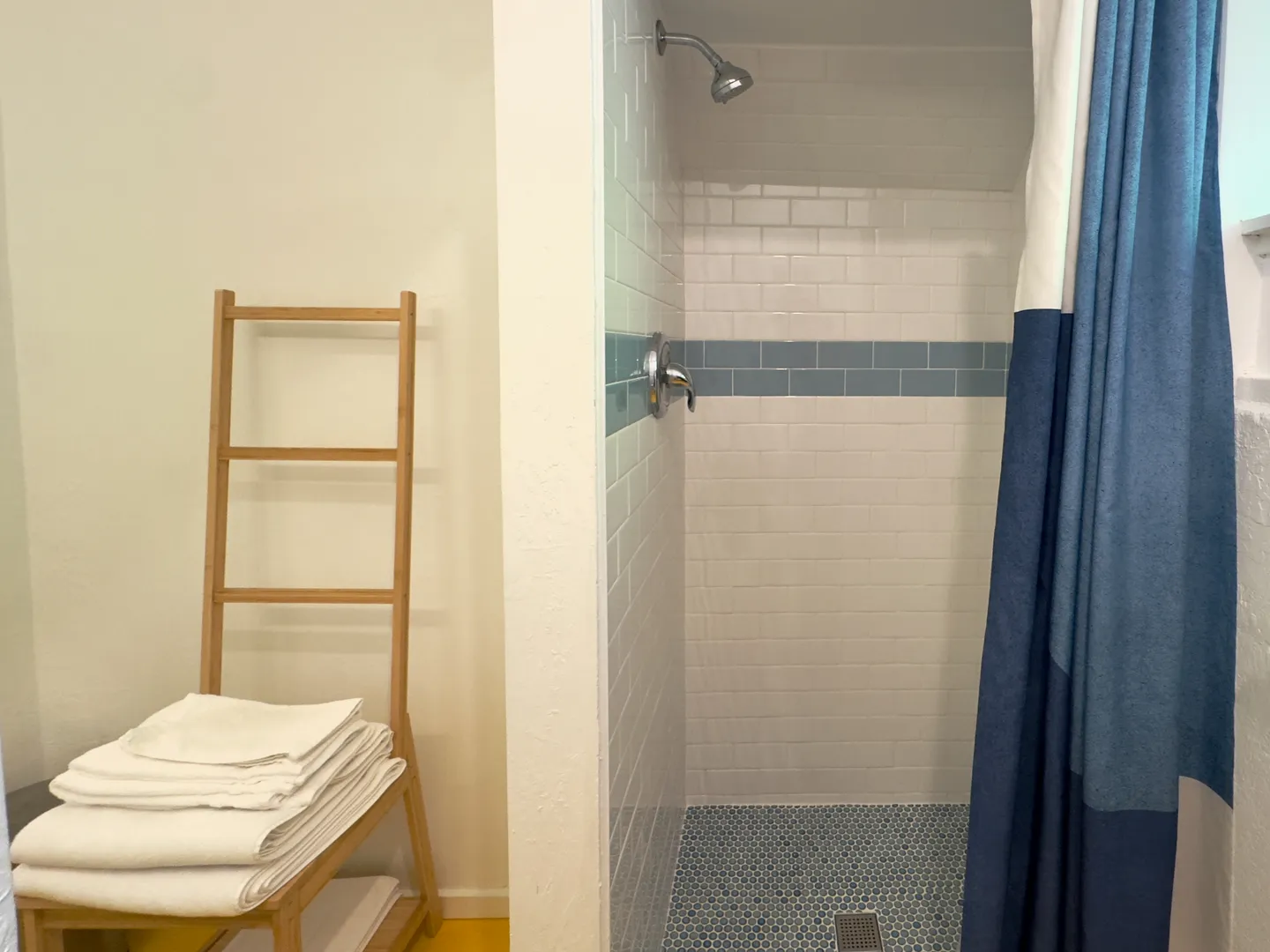 Walk-in shower with white subway tiles and a blue accent stripe alongside a wooden towel ladder.