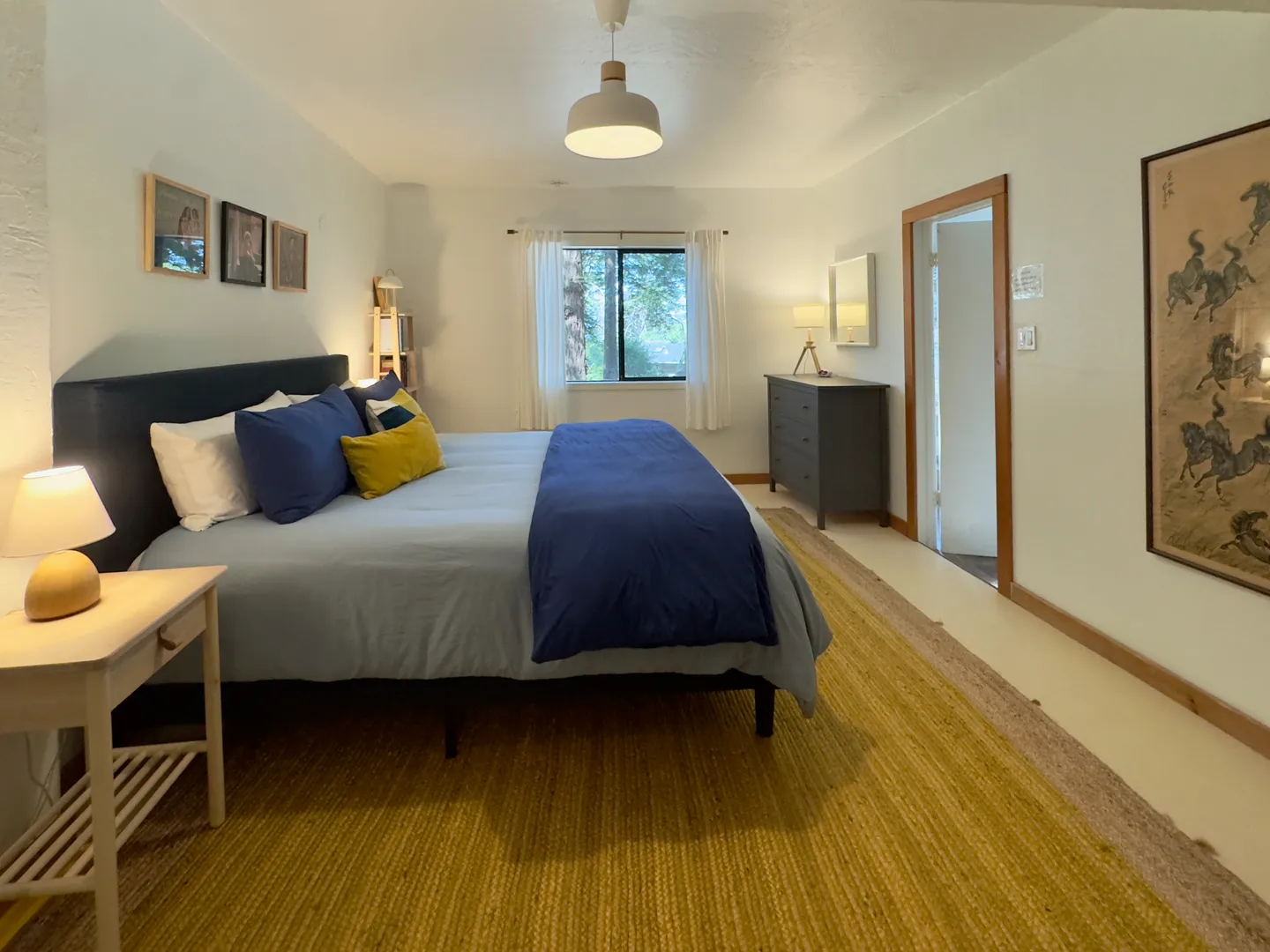 Bedroom with a large bed made with blue bedding, a yellow area rug, nightstand, and a window.
