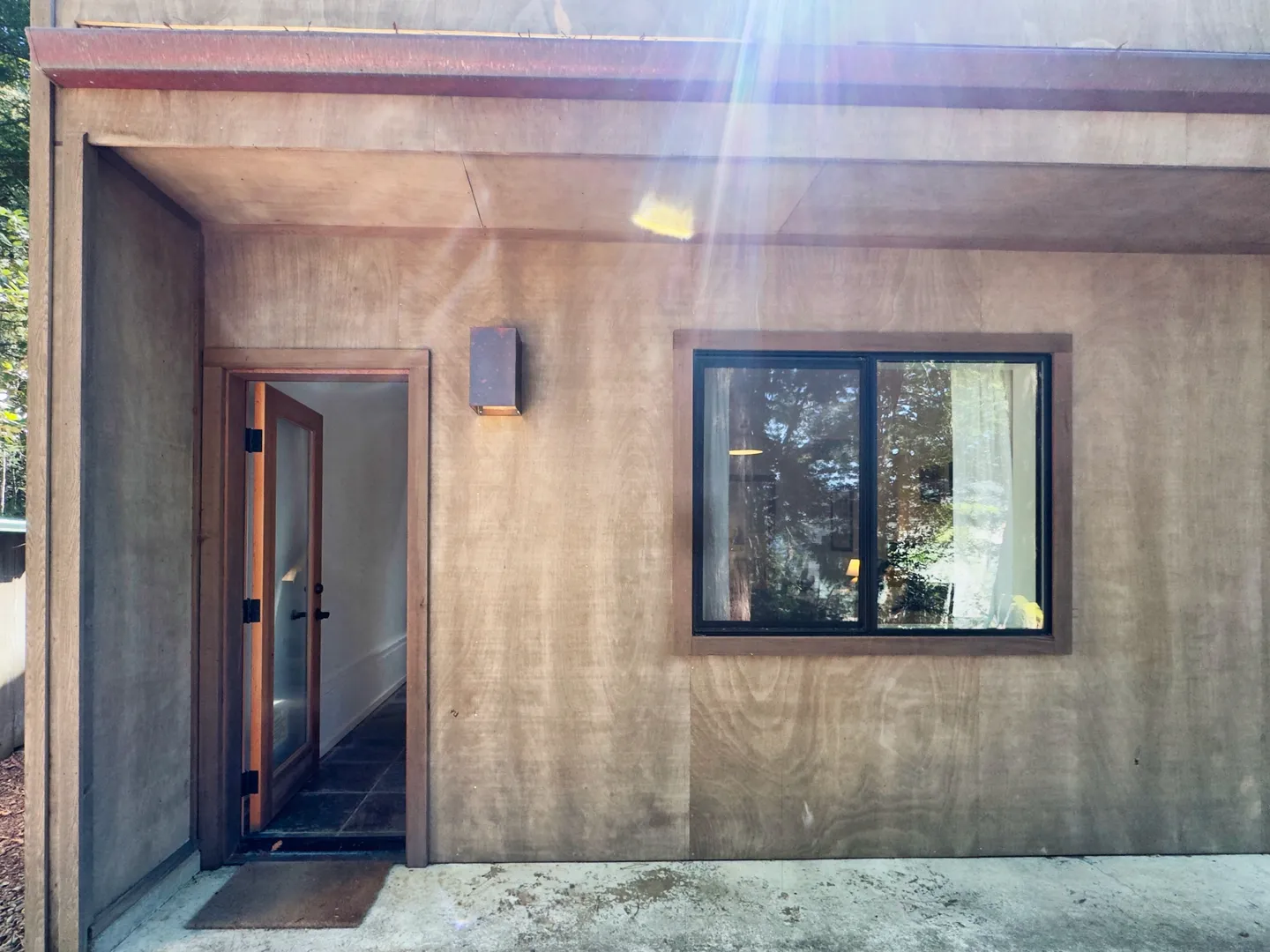 Exterior doorway and window set into a wood-paneled wall beneath an overhanging roof.
