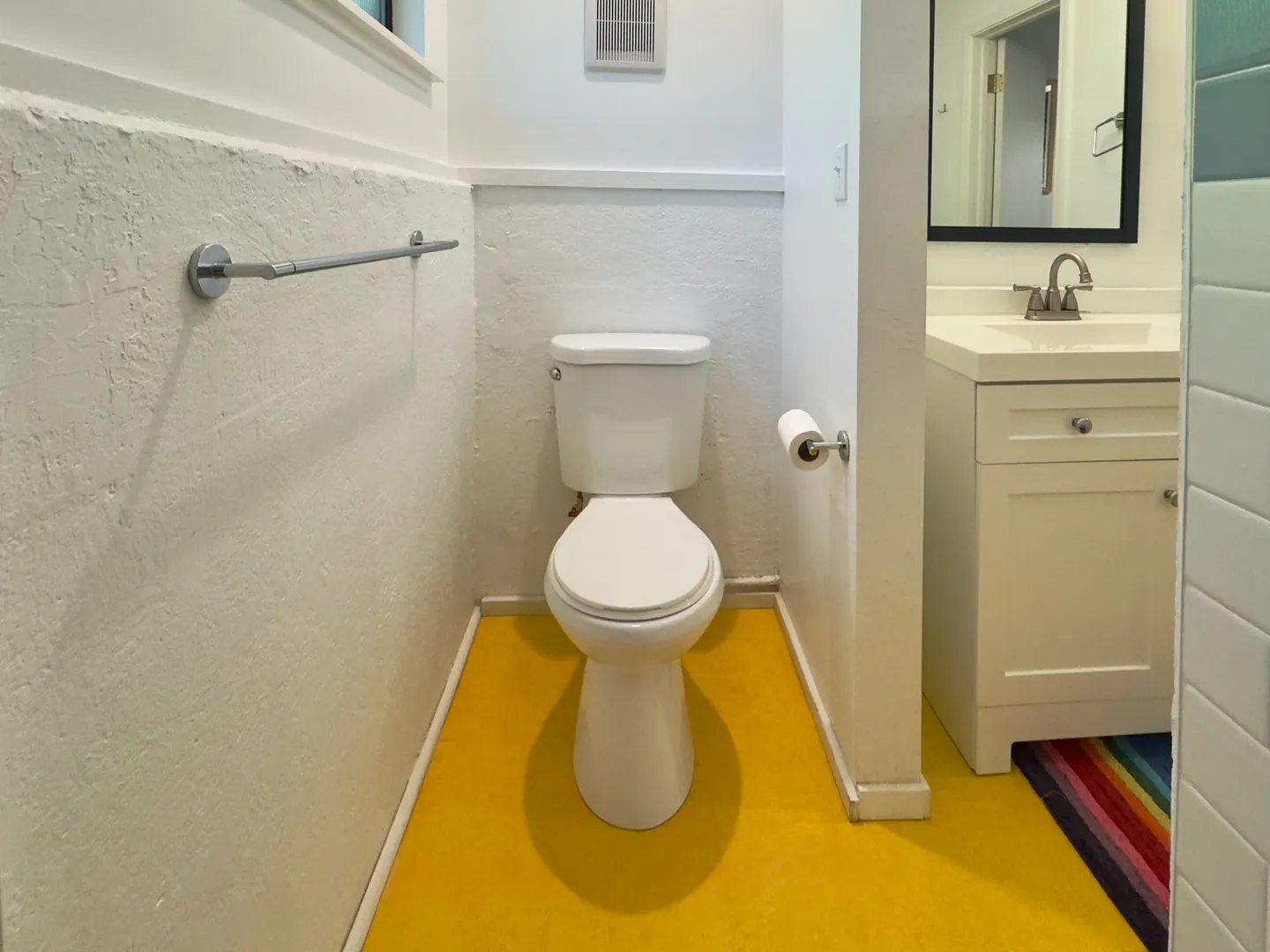 Bathroom featuring bright yellow flooring, a white toilet in an alcove, and an adjacent vanity with sink and mirror.