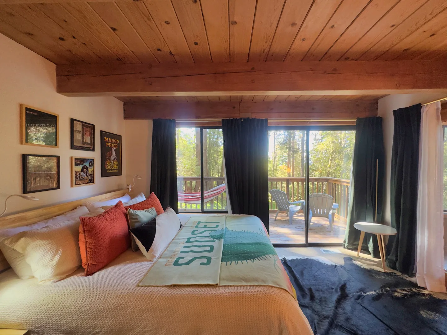 Bedroom with a wood-beamed ceiling and sliding glass doors that open to an outdoor deck surrounded by trees.